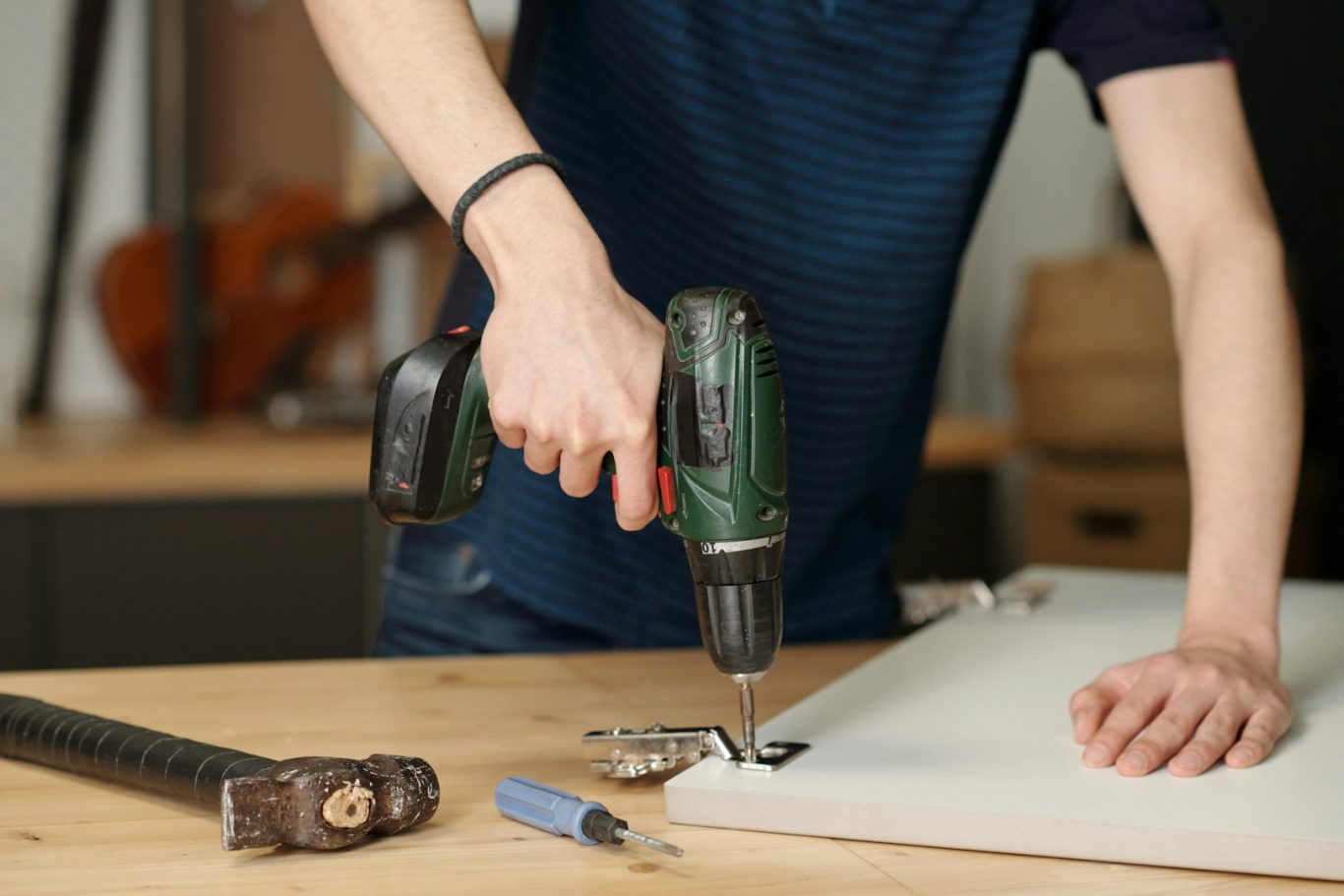 Montagearbeiten Person verwendet einen Akku-Bohrer, um ein Blatt Holz zu befestigen. Werkzeug und Schrauben sichtbar.