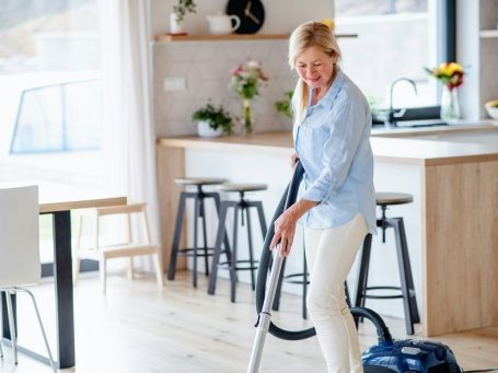 Eine Frau mit einem Staubsauger reinigt einen hellen Wohnraum.