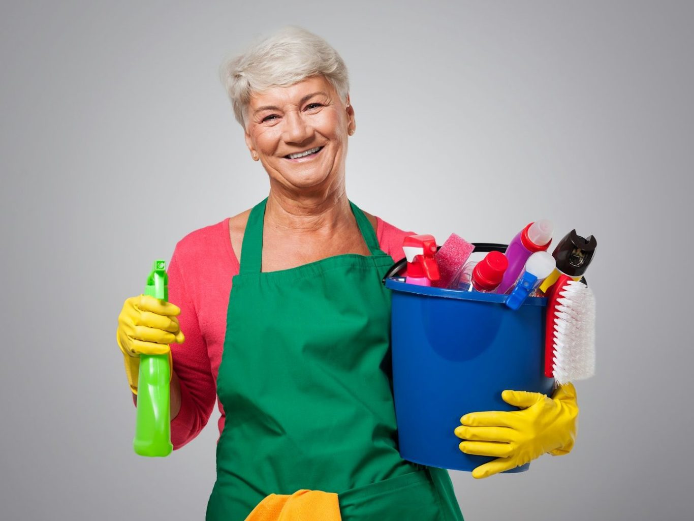 Ältere Frau mit grauen Haaren, die Reinigungsmittel in einer blauen Box hält und lächelt.
