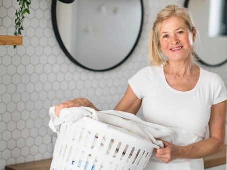 Eine lächelnde Frau hält einen Wäschekorb in einem modern gestalteten Raum.