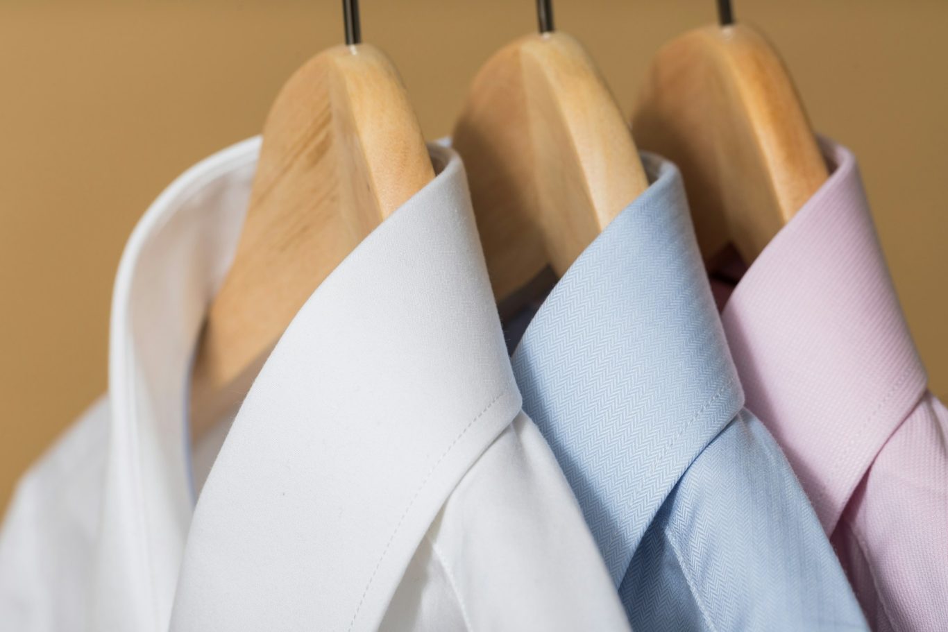 Gebügelte Hemden Drei Hemden in Weiß, Hellblau und Rosa hängen an Holzkleiderbügeln.