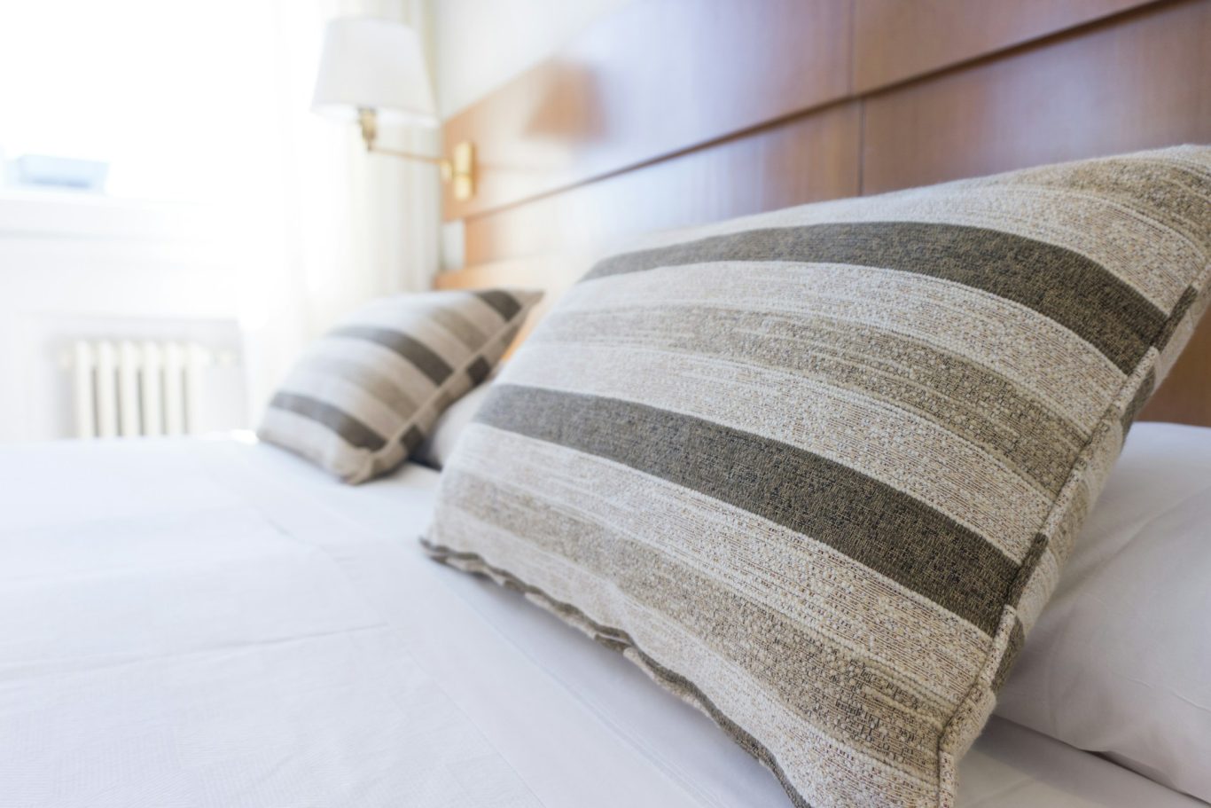 Kingsizebett Gestreifte Kissen auf einem Bett mit heller Bettwäsche in einem Schlafzimmer.